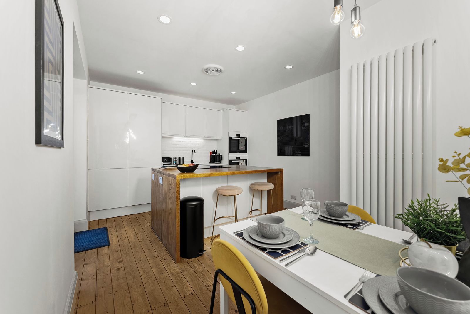 A modern kitchen with white cabinets, a wooden island, and a dining area with a table set for two.