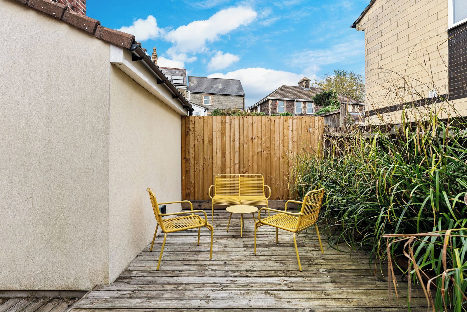 A patio with a wooden deck, two yellow chairs, and a small round table.