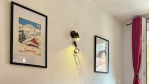 A room with a bed, a framed picture of a mountain, a wall-mounted light, and a window with red curtains.