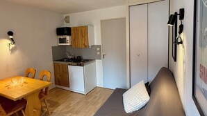 A compact living space with a kitchenette, a dining area, and a sofa with pillows.