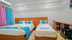 A hotel room with two beds, a wooden headboard, and a small desk with a refrigerator. - CLUB ROOM , (Bhubaneswar)
