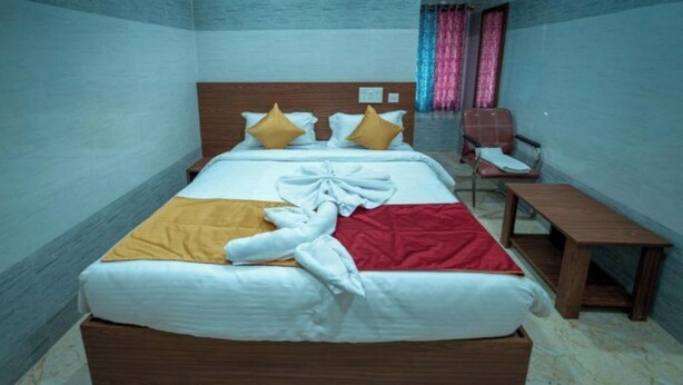 A hotel room with a bed, a wooden nightstand, a chair, and a small table. - CLUB ROOM , (Bhubaneswar)