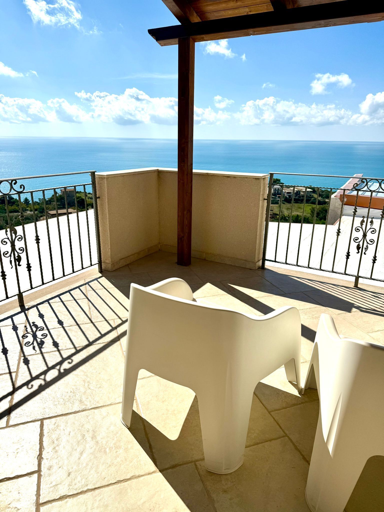 Un balcone con vista sul mare, sedie di plastica bianca e una struttura a pergola.