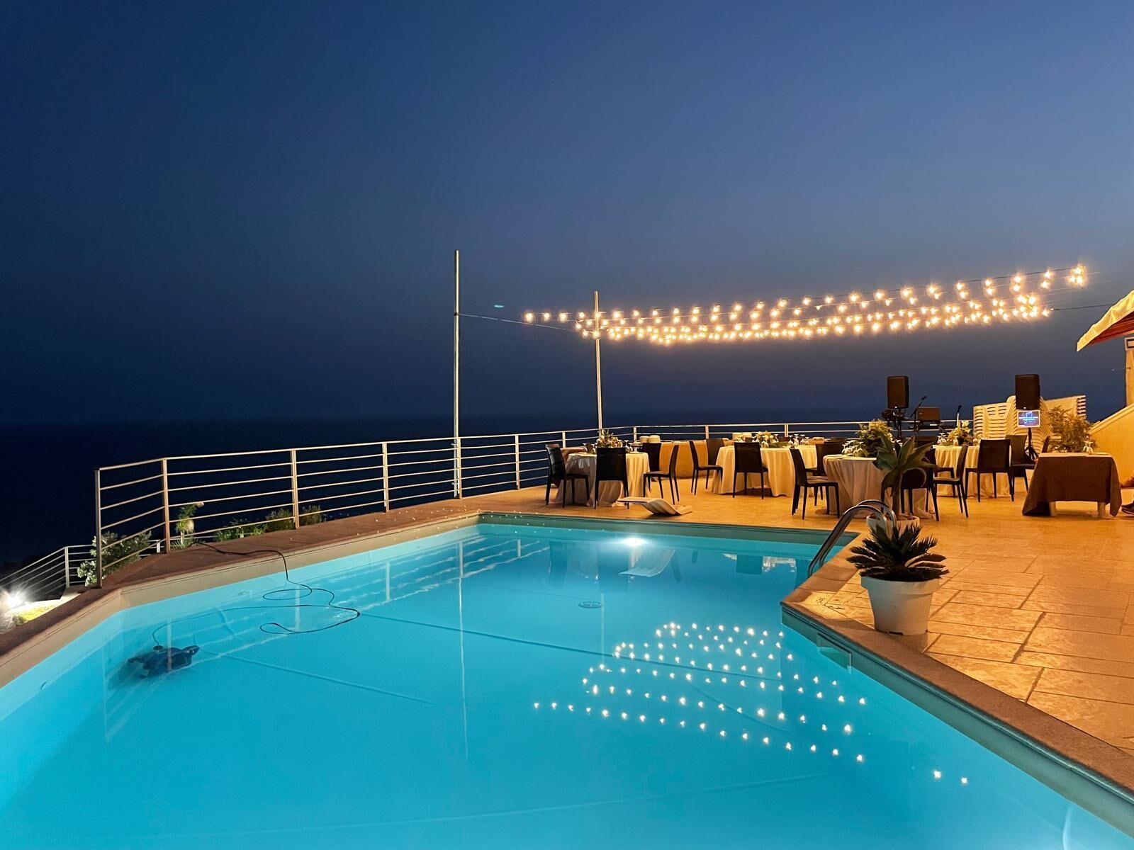 Ein Poolbereich mit Blick aufs Meer, Lichterketten und Sitzmöglichkeiten im Freien.