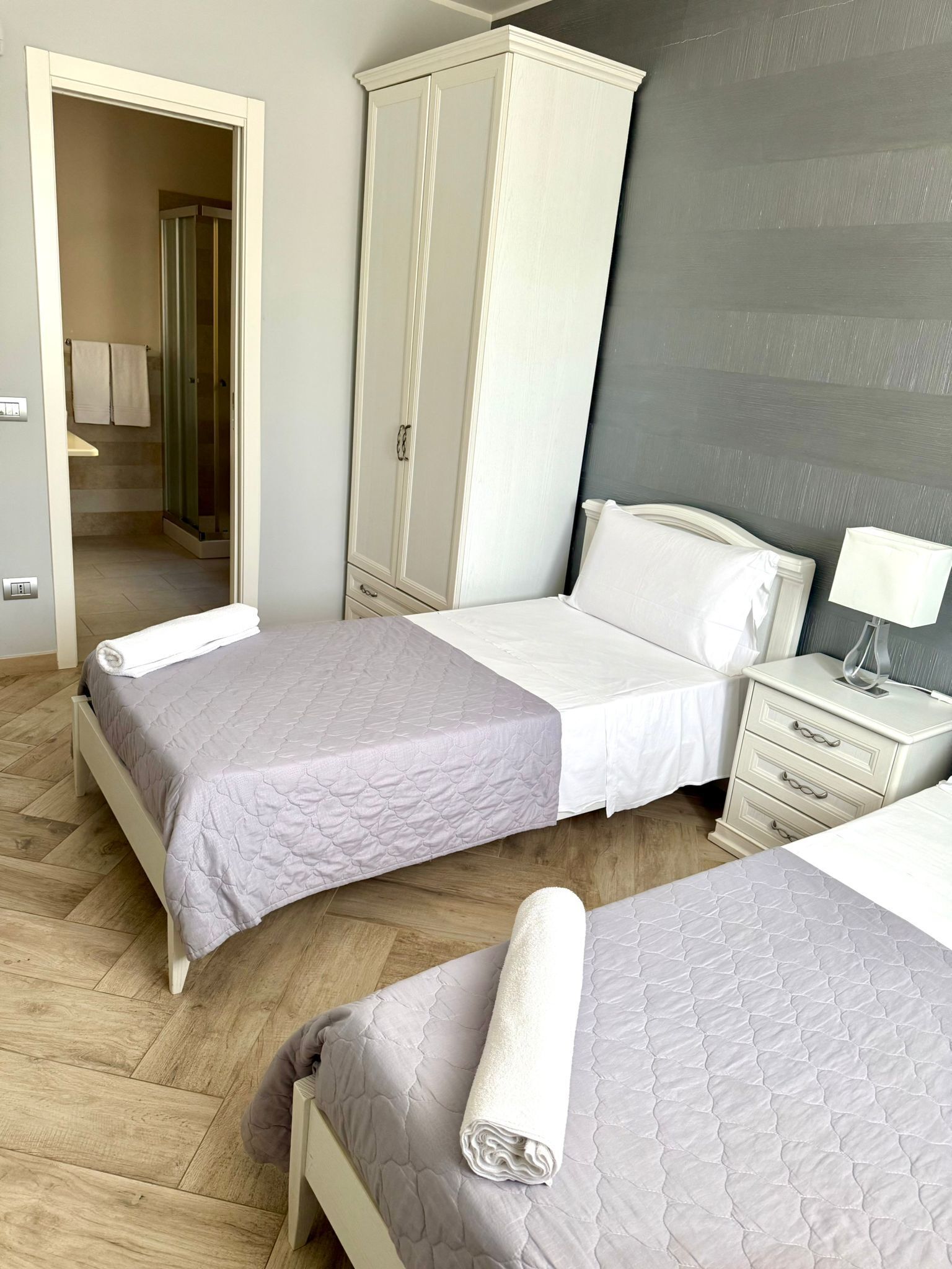 Une chambre avec deux lits, une armoire, une table de chevet et une salle de bain visible à travers une porte ouverte.