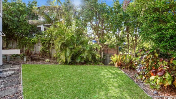 A well-maintained backyard with a lawn, various plants, and a wooden fence. - 10 Voyagers Place - Coastal Sanctuary (Sunrise Beach)