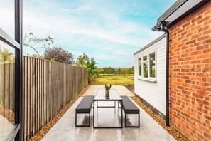 Een terras met een tafel en banken, een houten omheining en een bakstenen muur.