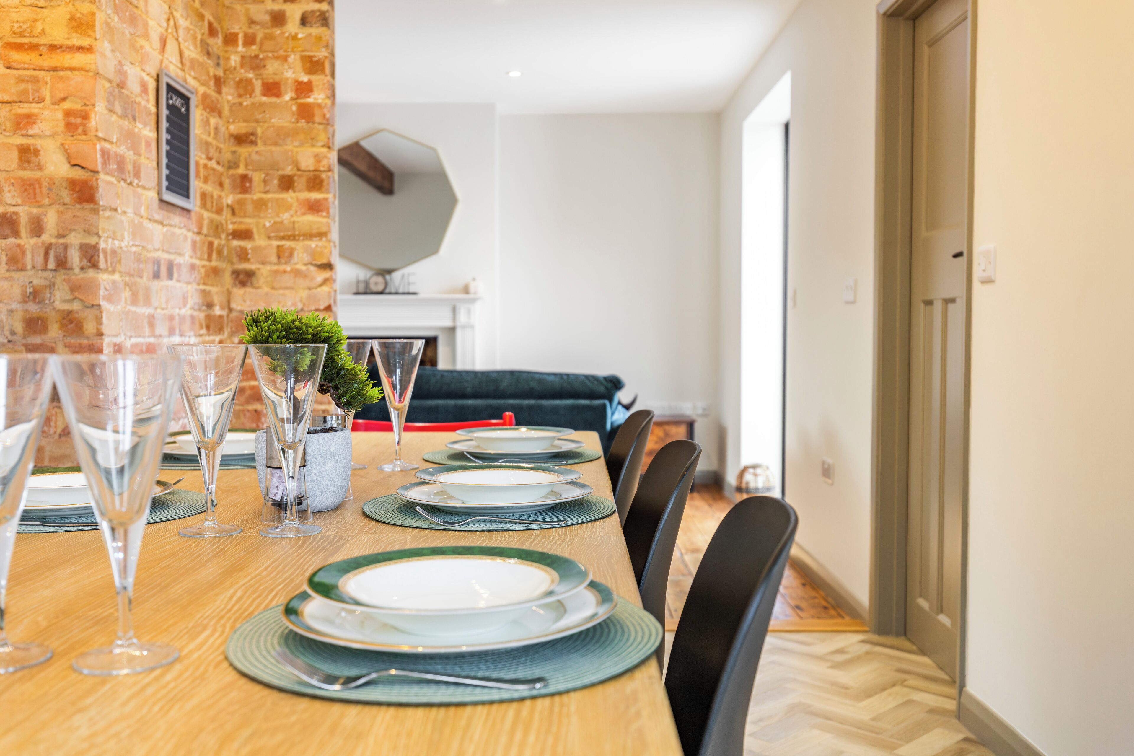 A dining table set with plates, glasses, and cutlery, with a brick wall and a sofa in the background.
