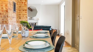 Una mesa de comedor dispuesta con platos, vasos y cubiertos, con una pared de ladrillo y un sofá al fondo.