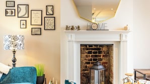 Una sala de estar acogedora con chimenea, una mesa de centro con pasteles y un sillón azul.