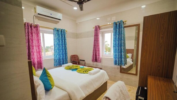 A hotel room with a bed, a chair, a mirror, and a ceiling fan.