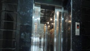 An elevator with a glass door, a digital display, and a marble wall.