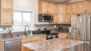 A modern kitchen with wooden cabinets, stainless steel appliances, granite countertops, and pendant lighting.