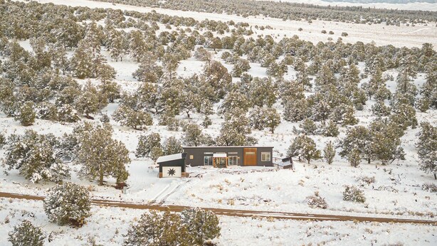 A modern house surrounded by a snowy landscape with mountains in the background.
