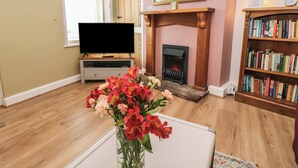 Un salon avec une cheminée, un téléviseur, une bibliothèque et un vase de fleurs.