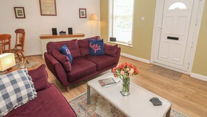 Un salon avec un canapé rouge, une table basse blanche et un vase rempli de fleurs. On y trouve également une chaise en bois et une petite table sur laquelle sont posées des haut-parleurs.