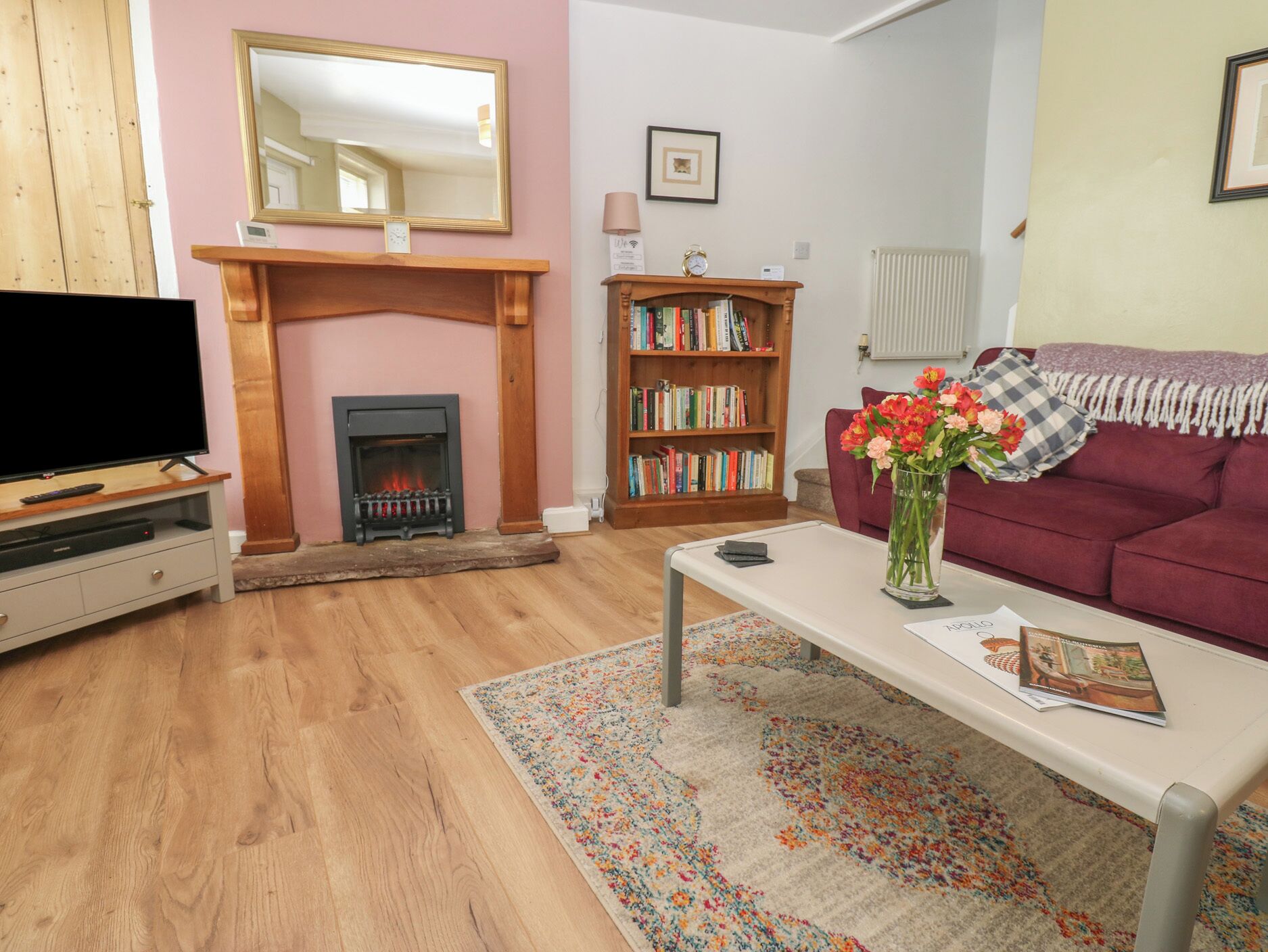 Ein Wohnzimmer mit Kamin, Fernseher, Bücherregal, Sofa und Couchtisch mit Blumenvase.