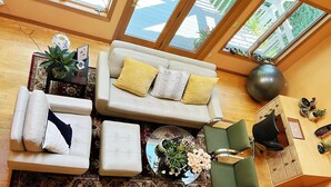 Un salon moderne avec un canapé, un pouf et un fauteuil vert, une table basse ornée d’un vase de fleurs et un meuble en bois contenant des objets décoratifs.
