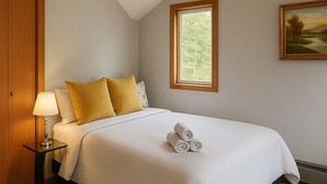Un lit bien fait, avec du linge de lit blanc et des serviettes pliées, une lampe de chevet et un tableau accroché au mur.