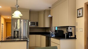 Une cuisine compacte équipée d’un réfrigérateur, d’un four à micro-ondes, d’une machine à café et d’un petit coin repas avec une table et une chaise.