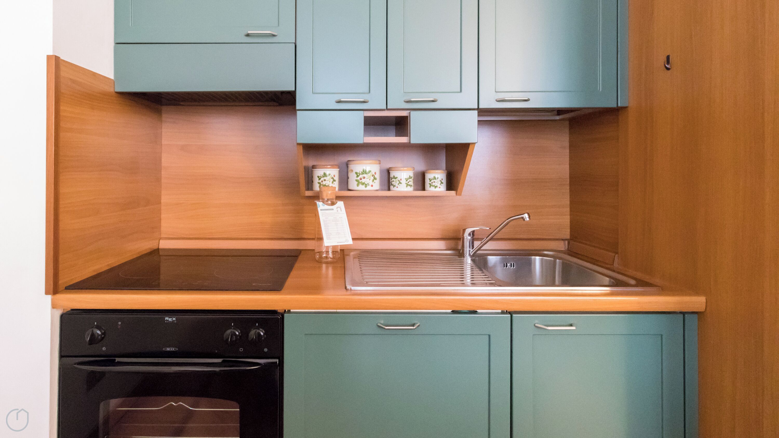 A kitchen with teal cabinets, a stainless steel sink, and a black oven.