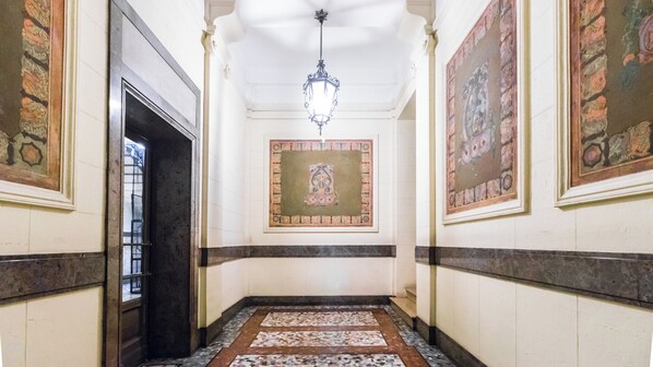 A hallway with a patterned floor, a hanging light fixture, and framed artwork on the walls.