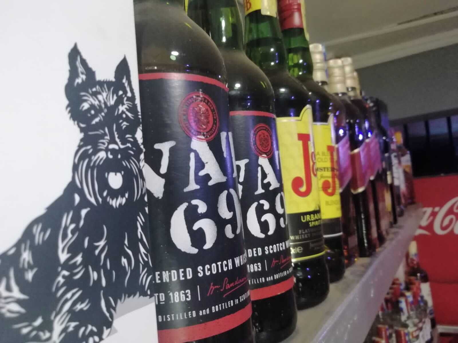 A row of whisky bottles with labels, including one with a cat illustration and another with a red and black label.