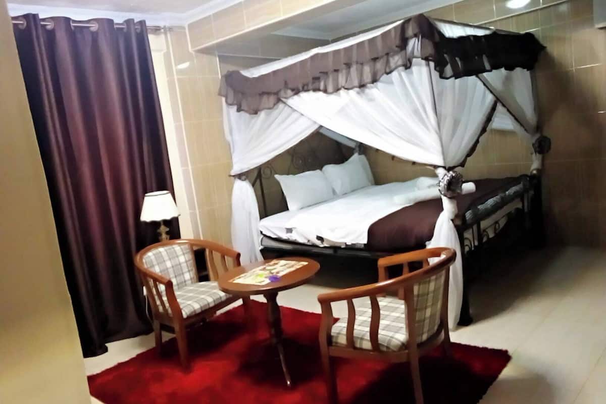 Una cama individual con dosel, dos sillas, una mesita y una alfombra roja en una habitación de hotel.