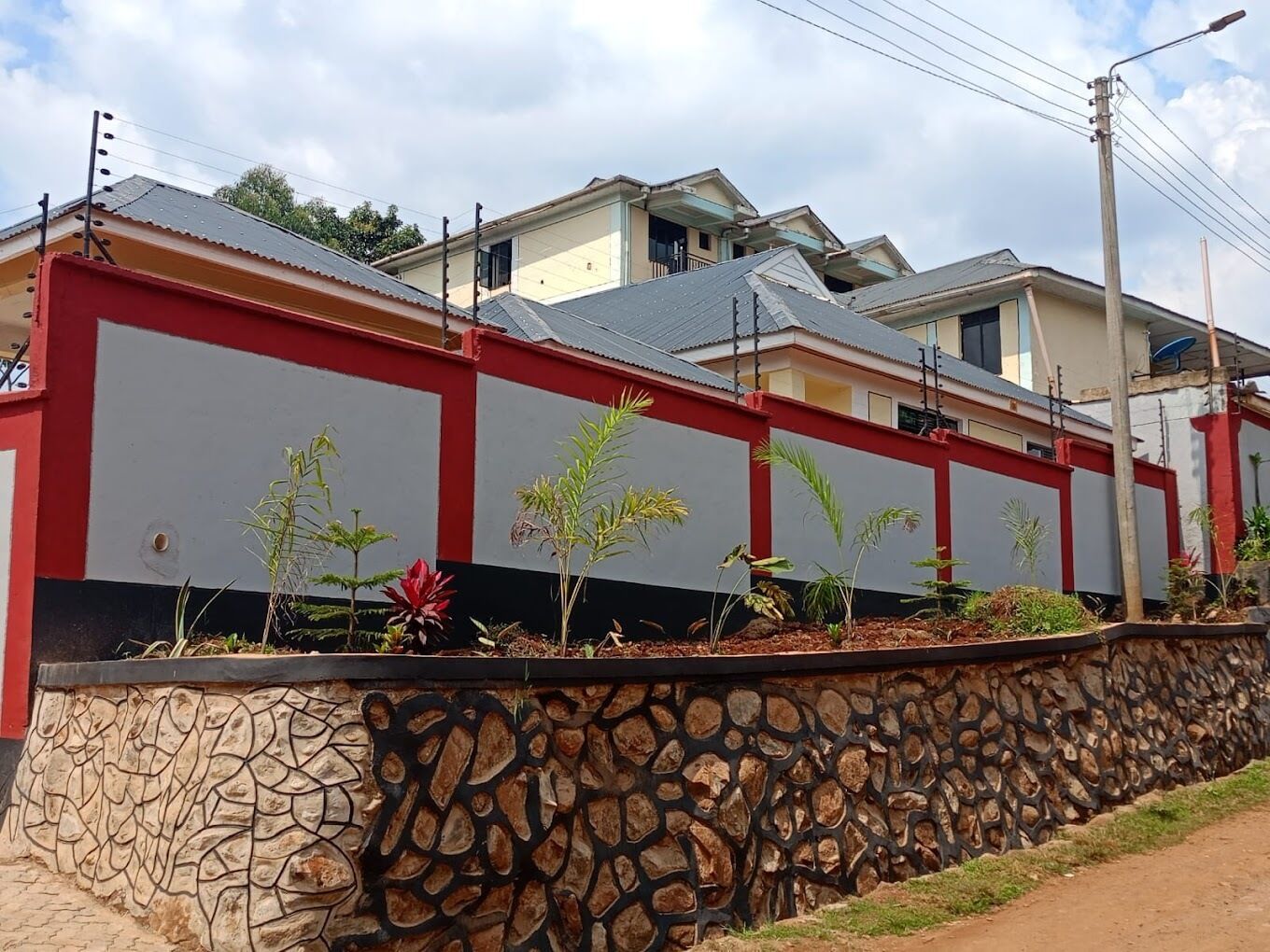 A residential building with a stone wall and small plants in front.