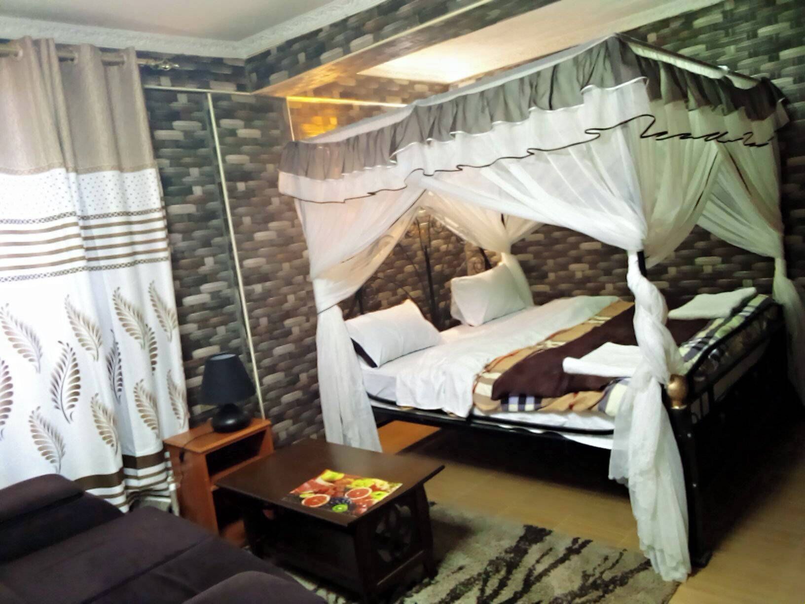 A bedroom with a canopy bed, a small bedside table, a decorative rug, and a sofa.