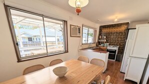 A dining area with a wooden table and chairs, a bowl on the table, and a kitchen in the background. - Gwendoline Cottage, Pets, Main St. Station (Croydon)