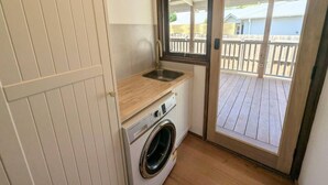 A compact bathroom with a washing machine, a sink, and a sliding glass door leading to an outdoor deck. - Gwendoline Cottage, Pets, Main St. Station (Croydon)