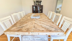 A rectangular dining table with a rustic finish, surrounded by white chairs. - Sandy`s Retreat- wineries, sanctuary, pets,main st (Healesville)