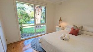 A bedroom with a large window, a bed with white bedding, a nightstand, and a lamp. - Sandy`s Retreat- wineries, sanctuary, pets,main st (Healesville)