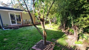 Un patio trasero con un árbol pequeño, una jardinera de ladrillo y una casa con puerta corrediza de vidrio.