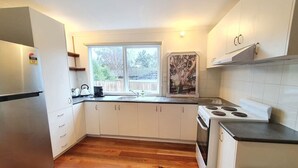 Cocina compacta con armarios blancos, un refrigerador de acero inoxidable, una estufa y un ventanal que proporciona luz natural.