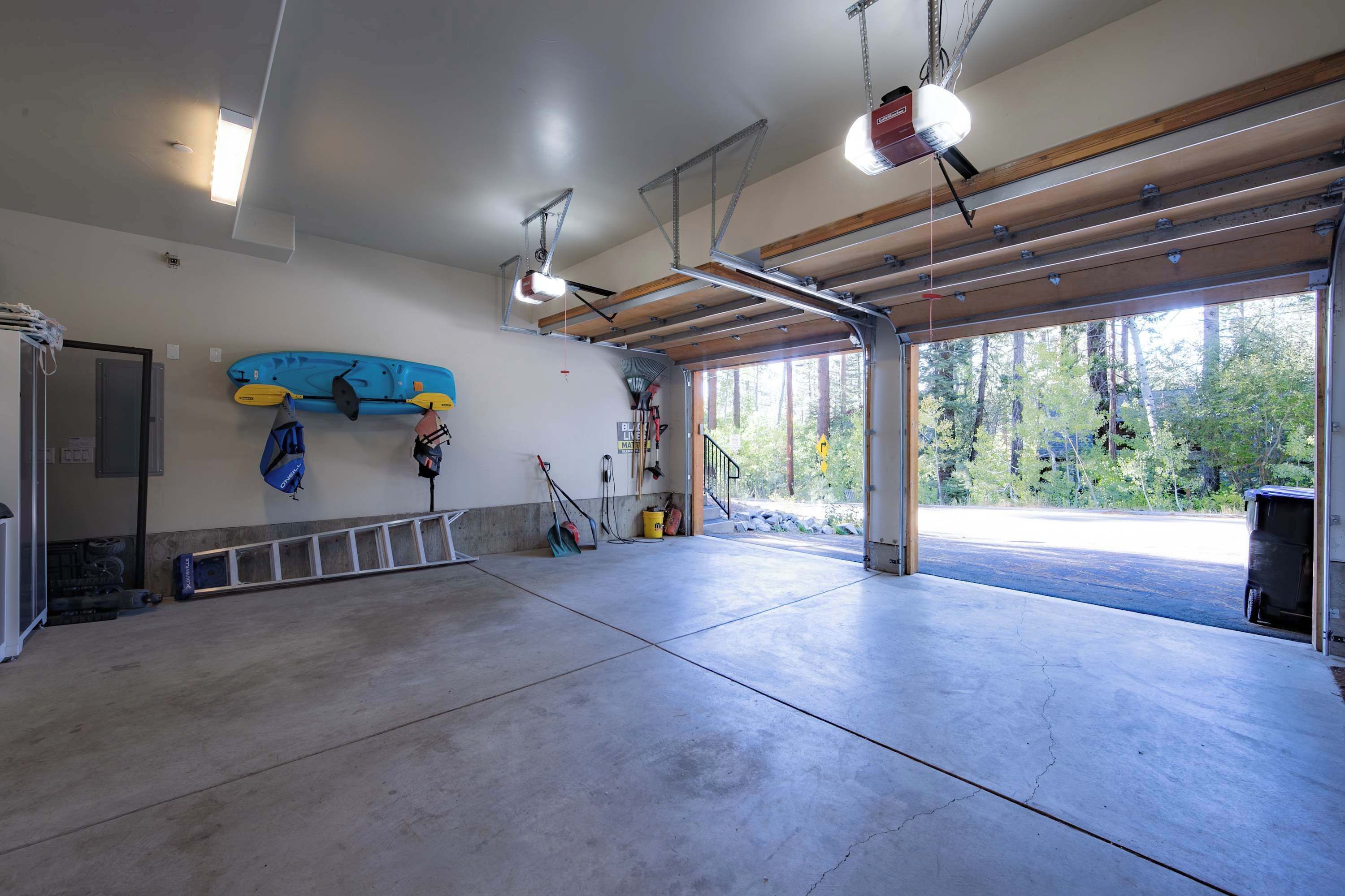 A spacious garage with a concrete floor, a kayak and paddleboards mounted on the wall, and a large window providing a view of the outdoors.