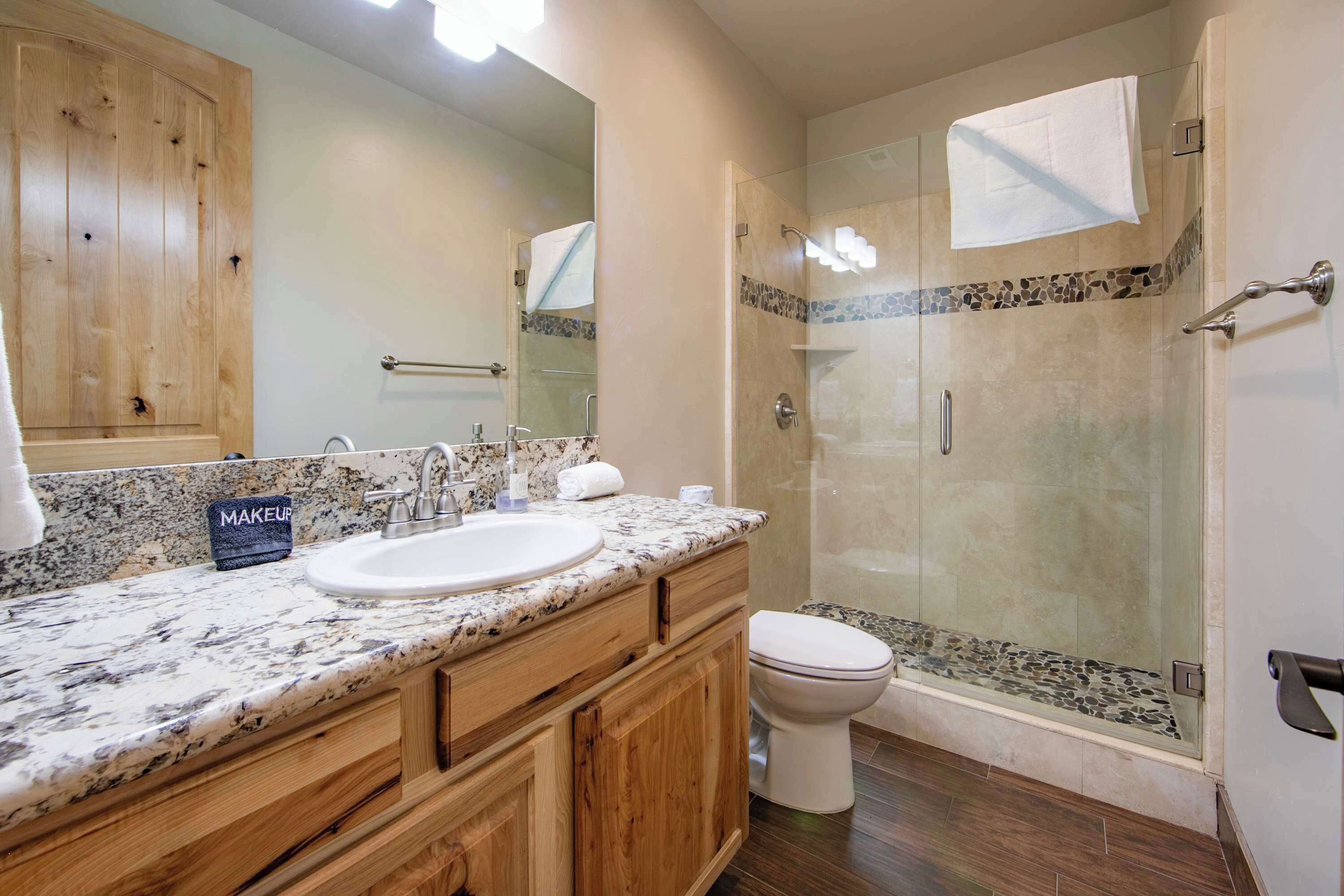 A bathroom with a granite countertop sink, wooden cabinets, a glass shower enclosure, and a white toilet.