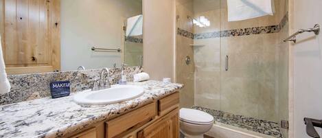 A bathroom with a granite countertop sink, wooden cabinets, a glass shower enclosure, and a white toilet.