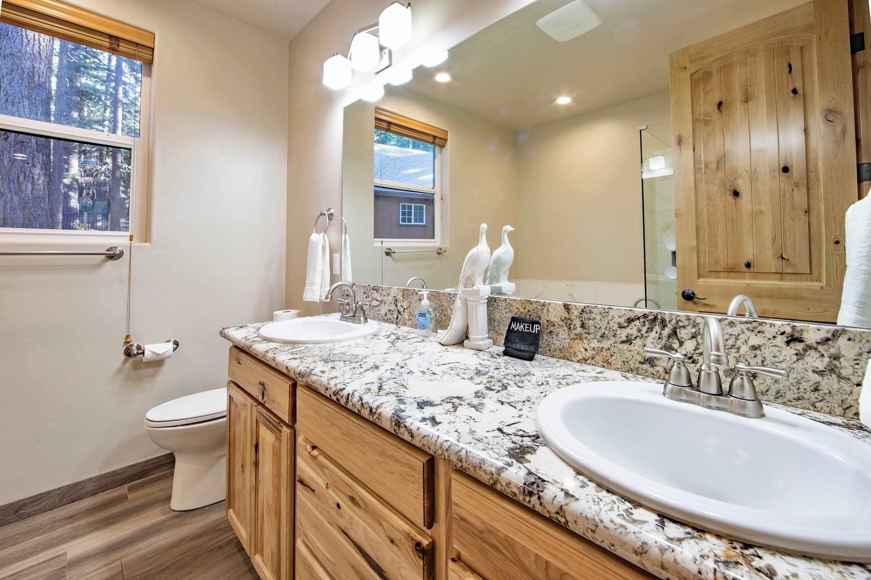 A bathroom with two sinks, wooden cabinets, a large mirror, and a window with a view of trees.