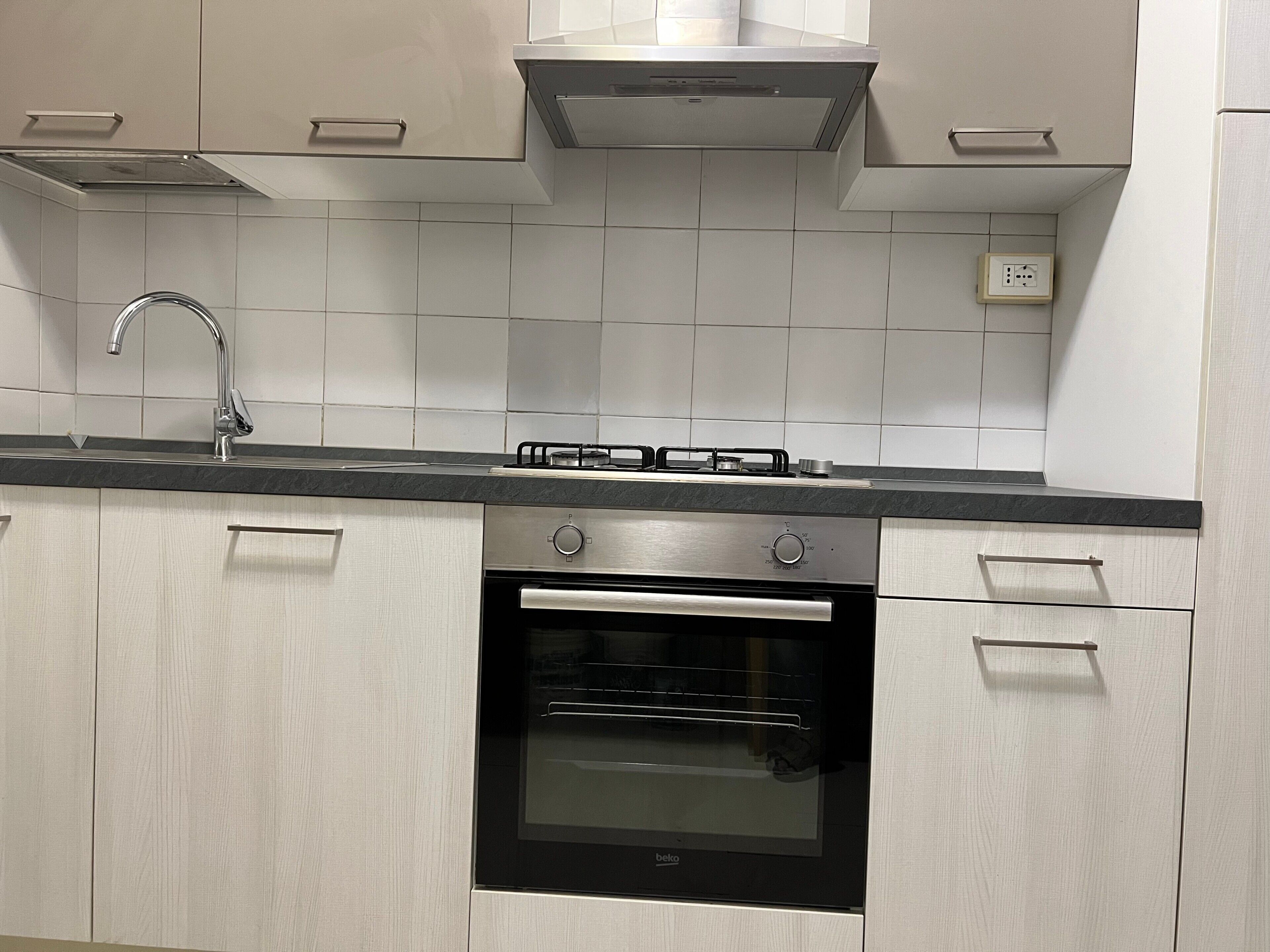 A kitchen with a stainless steel range hood, a built-in oven, and a modern faucet.