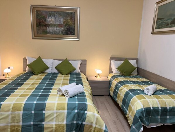 Une chambre d’hôtel avec deux lits, chacun recouvert d’une couvre-lit à carreaux, agrémenté d’oreillers verts et de lampes de chevet.