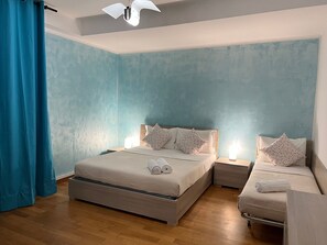 Une chambre avec deux lits, une table de chevet, un ventilateur de plafond et un rideau bleu.