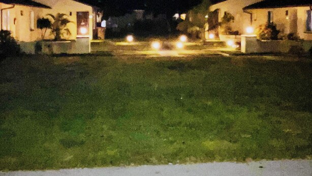 Vista nocturna de una zona residencial con dos casas, cada una con un porche visible y un jardín delantero.