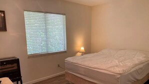 Un dormitorio con cama, mesita de noche, lámpara y ventana con persianas.