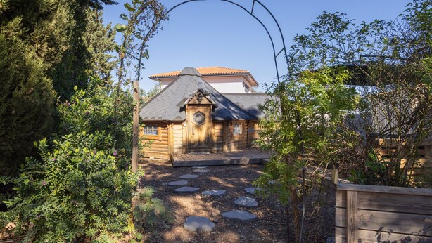 Une cabane en rondins avec un sentier de pierres menant à l’entrée, entourée d’un feuillage dense.