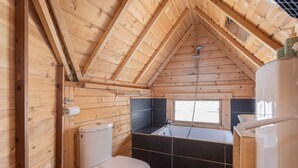 Une cabane en bois avec un plafond en pente, des toilettes, une baignoire et une fenêtre.