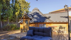 Une cabane en rondins avec un toit hexagonal, une terrasse en bois et un canapé bleu.