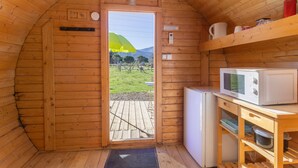 A wooden cabin interior with a kitchen area, a door leading outside, and a view of a grassy field. - Barrel Orange Apartment with Mountain View, Private Terrace & Air Conditioning (Saint André)