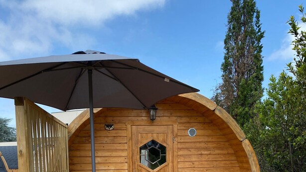 A wooden cabin with a hexagonal window, a door, and a small porch with a table and chairs. - Barrel Orange Apartment with Mountain View, Private Terrace & Air Conditioning (Saint André)